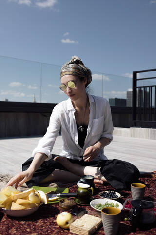 Stilvolle Frau mit Sonnenbrille bei einer gesunden Mahlzeit auf dem Dach, lizenzfreies Stockfoto