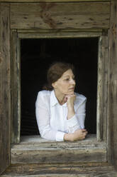 Frau schaut aus dem Fenster eines alten Holzhauses - AHSF00797