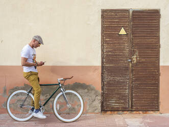 Mann mit Fixie-Fahrrad schaut auf sein Handy - DLTSF00049