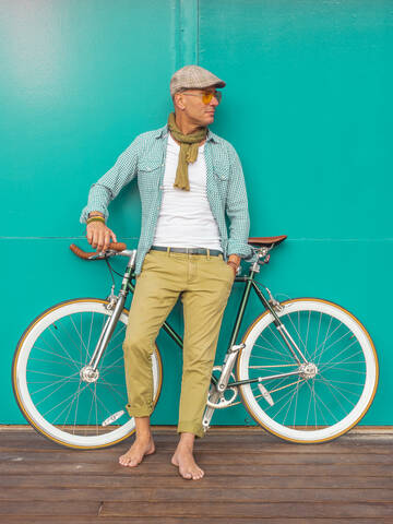 Barfußmann mit Fixie-Fahrrad vor grüner Wand stehend, lizenzfreies Stockfoto