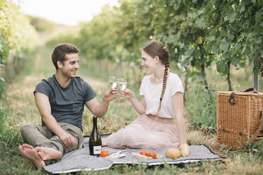 Glückliches junges Paar beim Picknick in den Weinbergen, das mit Prosecco anstößt - ALBF01019