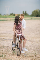 Küssendes Paar mit handgefertigtem Rennrad auf einem Stoppelfeld - ALBF01048