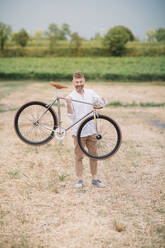 Man with handcrafted racing cycle on stubble field - ALBF01049