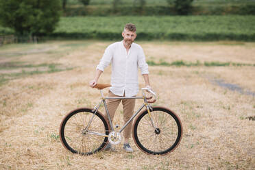 Man with handcrafted racing cycle on stubble field - ALBF01050