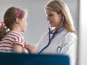 Female doctor listening to a young girl heart using a stethoscope in a clinic - ABRF00618