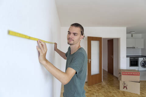 Young man measuring the wall in an empty apartment stock photo