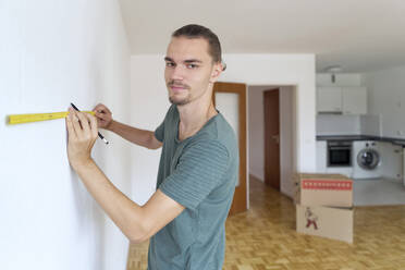 Junger Mann misst die Wand in einer leeren Wohnung - FLLF00284