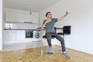 Young man taking a selfie with his smartphone in an empty apartment - FLLF00285