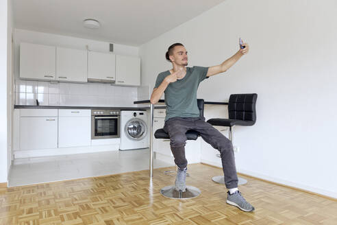 Junger Mann macht ein Selfie mit seinem Smartphone in einer leeren Wohnung - FLLF00285