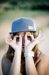 Frau mit Mütze, die durch ihre Finger schaut, in Form eines Fernglases - OCMF00613