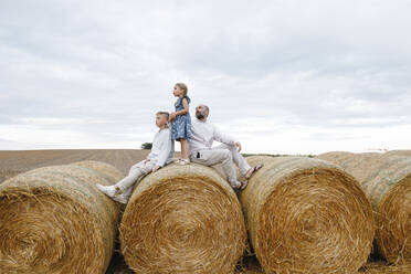 Father and his children sitting on hay bales, watching sky - KMKF01078