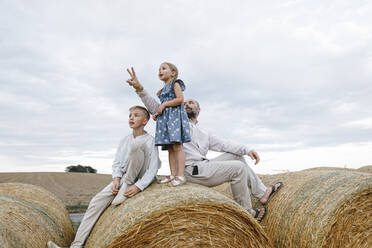 Father and his children sitting on hay bales, watching sky - KMKF01079