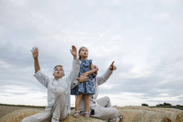 Father and his children sitting on hay bales, watching sky - KMKF01081