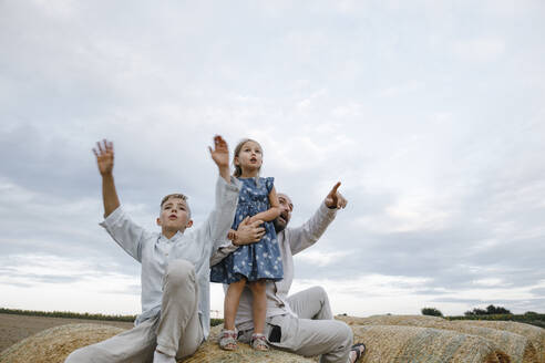 Vater und seine Kinder sitzen auf Heuballen und beobachten den Himmel - KMKF01081