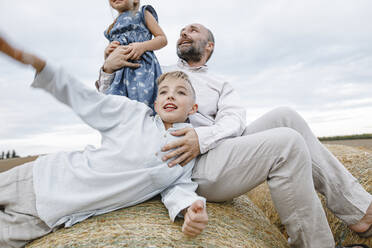 Father and his children playing and laughing on hay bales - KMKF01082