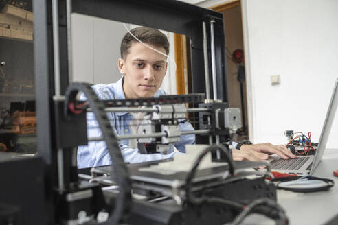 Student beim Einrichten eines 3D-Druckers mit Laptop - VPIF01461