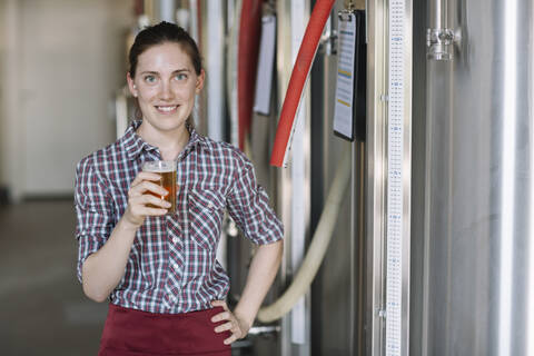 Porträt einer selbstbewussten jungen Frau mit einem Bierglas in einer Brauerei, lizenzfreies Stockfoto