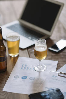 Beer bottle, glasses, documents and laptop on table - ALBF01081