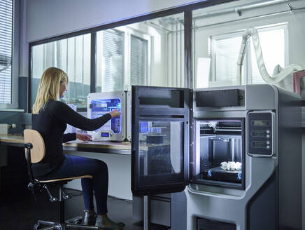 Female technician checking 3D printer with turbine wheel being printed - CVF01483