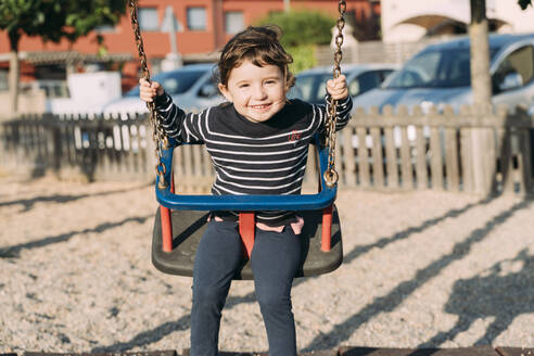 Porträt eines glücklichen kleinen Mädchens beim Schaukeln auf einem Spielplatz - GEMF03118