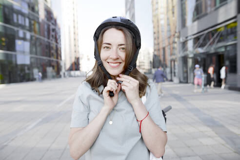 Frau setzt einen Helm auf, E-Scooter im Hintergrund - KMKF01087