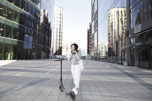 Frau mit E-Roller und Helm, moderne Gebäude im Hintergrund - KMKF01089