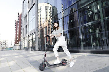 Frau mit E-Roller und Helm, moderne Bürogebäude im Hintergrund - KMKF01091
