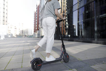 Junge Frau auf E-Roller, moderne Gebäude im Hintergrund - KMKF01094