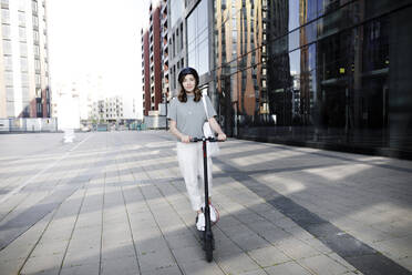 Woman with e-scooter and helmet, modern office buildings in the background - KMKF01095