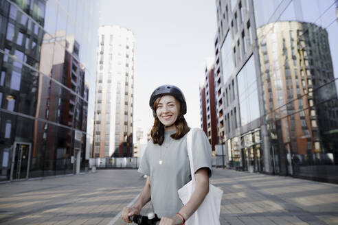 Frau mit E-Roller und Helm, moderne Bürogebäude im Hintergrund - KMKF01096