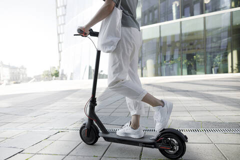 Young woman on e-scooter, modern buildings in the background stock photo