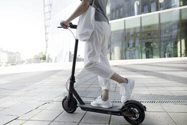 Young woman on e-scooter, modern buildings in the background - KMKF01097