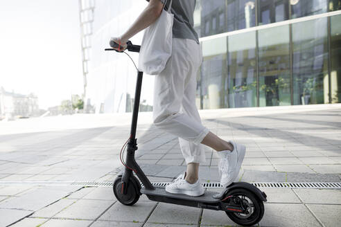 Junge Frau auf E-Roller, moderne Gebäude im Hintergrund - KMKF01097