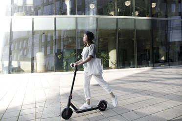 Frau mit E-Roller und Helm, moderne Bürogebäude im Hintergrund - KMKF01099