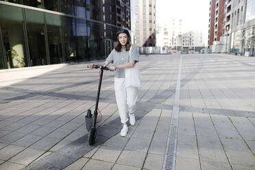 Woman with e-scooter and helmet, modern office buildings in the background - KMKF01102