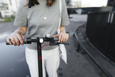 Frau mit E-Roller und Helm, die ein Smartphone benutzt, moderne Bürogebäude im Hintergrund - KMKF01119