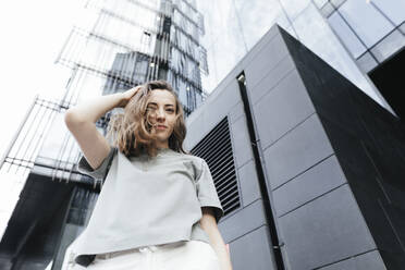 Portrait of smiling woman looking at camera, modern office buildings in the background, low angle view - KMKF01124