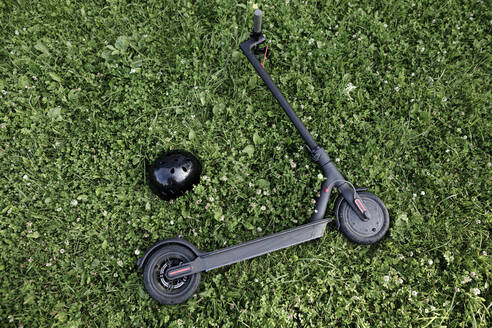 Electric scooter and helmet lying on meadow - KMKF01130
