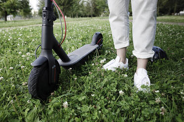 Frau mit E-Roller auf einer Wiese stehend - KMKF01131