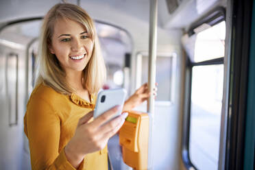 Smiling young woman using smartphone in a tram - BSZF01331