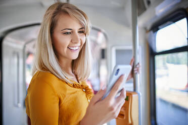 Smiling young woman using smartphone in a tram - BSZF01332