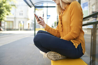 Nahaufnahme einer jungen Frau, die an einer Bushaltestelle ihr Smartphone benutzt - BSZF01338