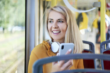 Lächelnde junge Frau mit Smartphone in einer Straßenbahn - BSZF01347