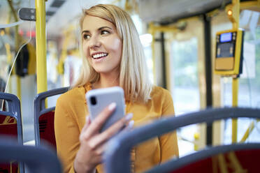 Lächelnde junge Frau mit Smartphone in einer Straßenbahn - BSZF01348
