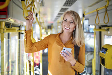 Smiling young woman with smartphone in a tram - BSZF01352