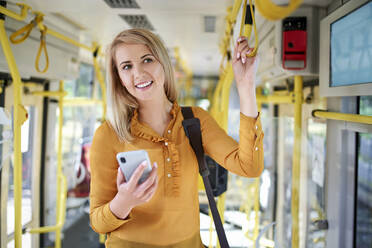 Lächelnde junge Frau mit Smartphone in einer Straßenbahn - BSZF01354