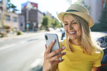 Glückliche junge Frau mit Smartphone in der Stadt - BSZF01361