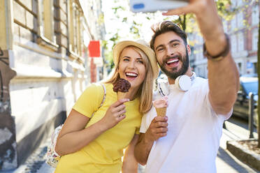 Glückliches junges Paar macht ein Selfie beim Eisessen in der Stadt - BSZF01369