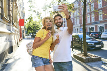 Glückliches junges Paar macht ein Selfie beim Eisessen in der Stadt - BSZF01370