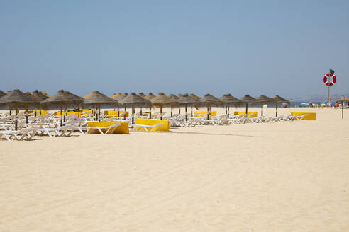 Strohdach-Sonnenschirme und Liegestühle am Strand gegen den klaren Himmel, Albufeira, Algarve, Portugal - WIF04018